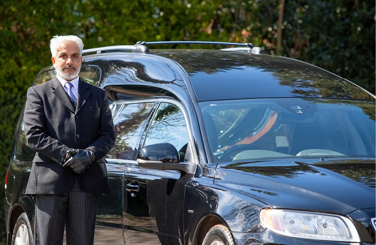 Photo of a funeral director standing next to a hearse